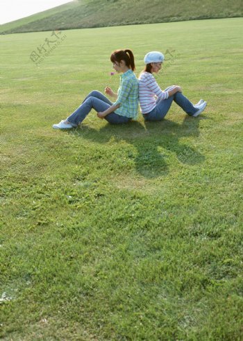 背靠背坐在草地上的两美女图片