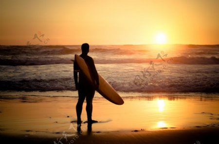 夕阳下拿着冲浪板的男人图片