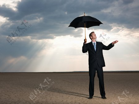站在沙漠中拿着伞等待下雨的外国男人图片
